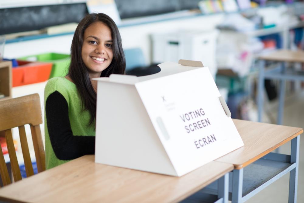 Student volunteer sitting next to vote submission box