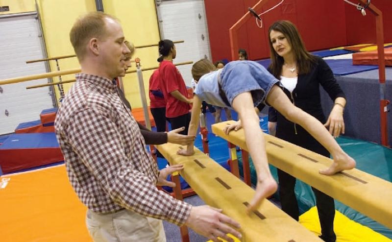 Two teachers teaching young student how to use gymnasium equipment