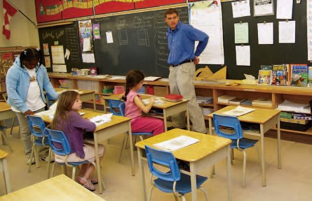 teacher standing in front of classroom while children are working