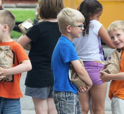 young elementary students standing together near school bus holding paper bags