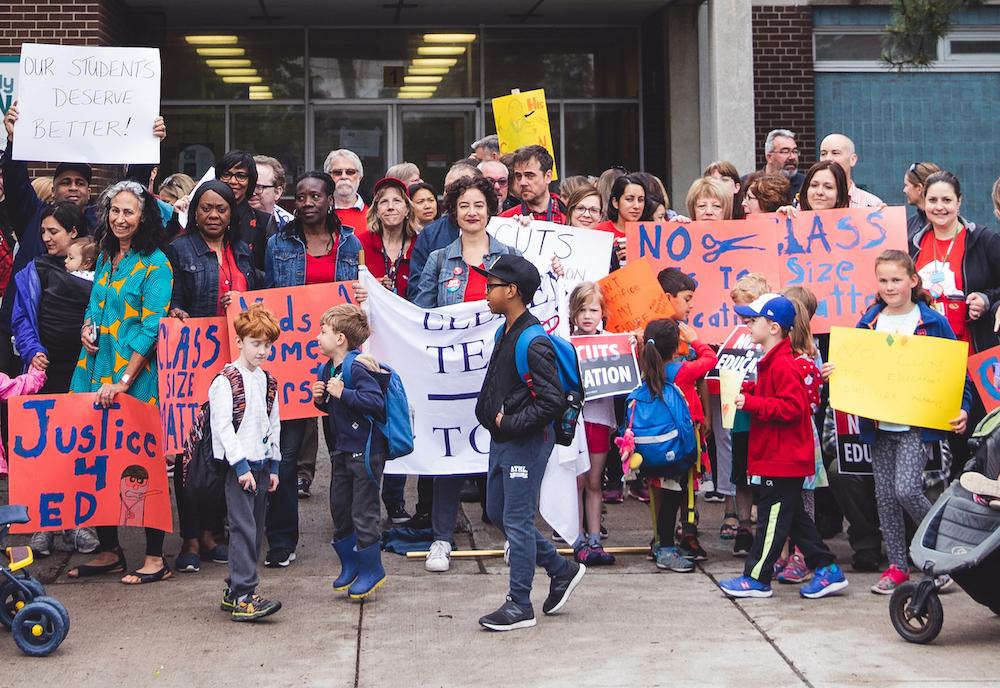 teachers and parents standing in front of school with signs