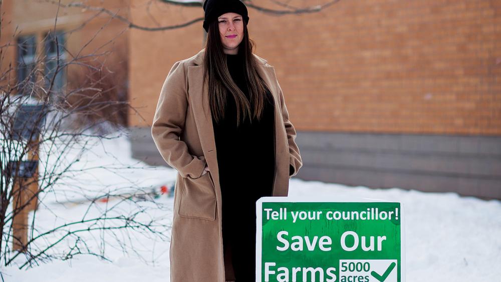 Sarah Lowes standing next to sign for saving farms