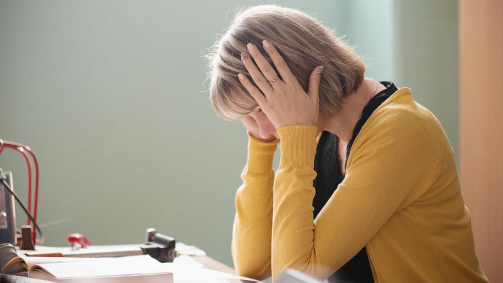 Woman with hands on head looking stressed while sitting in classroom