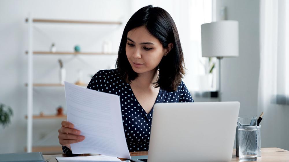 Woman sitting at laptop examining document