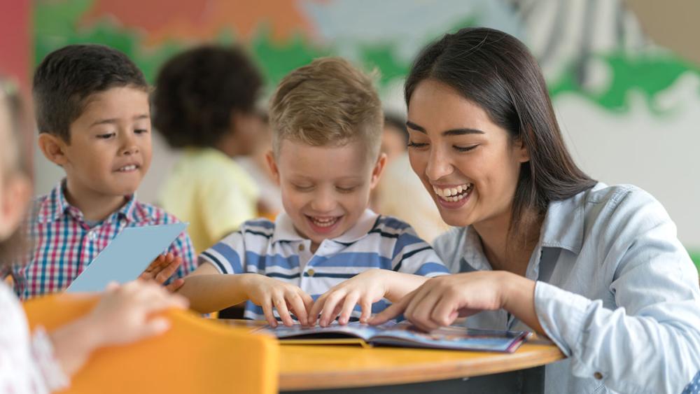 Woman teacher interacting with two kindergarten students with book