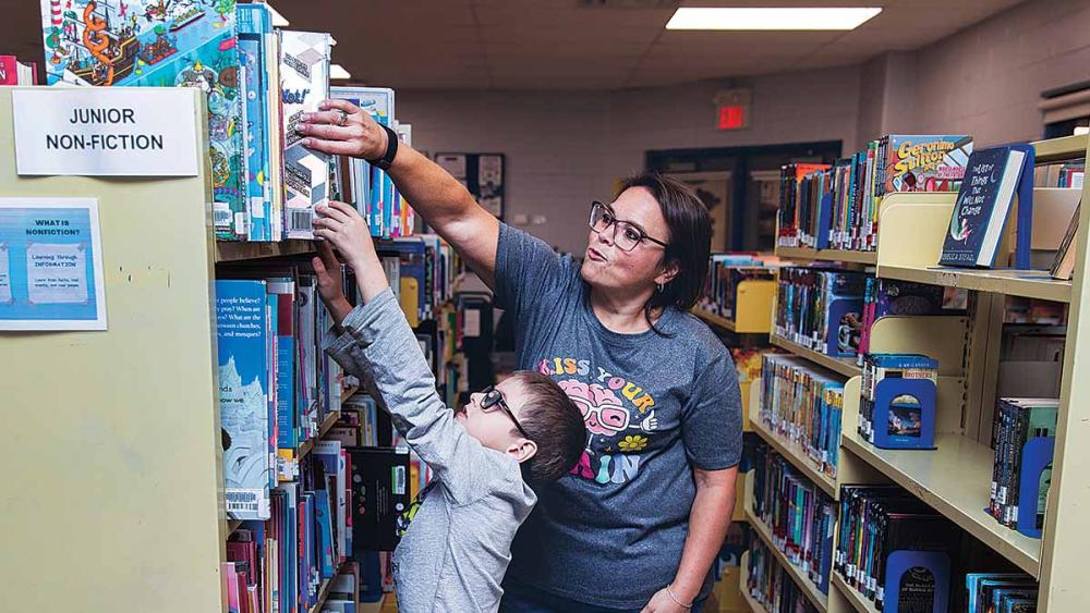 Nancy Campbell helping student put book on shelf in library