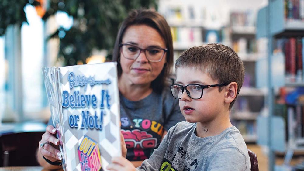 Nancy Campbell reading book with student in library