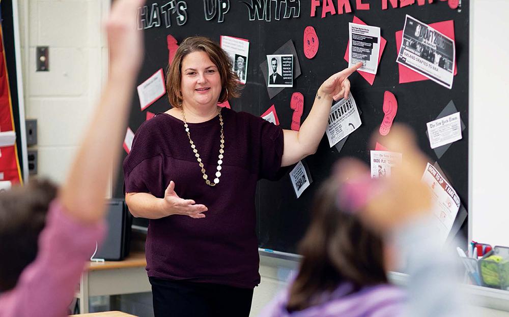 teacher in front of classroom pointing at fake news