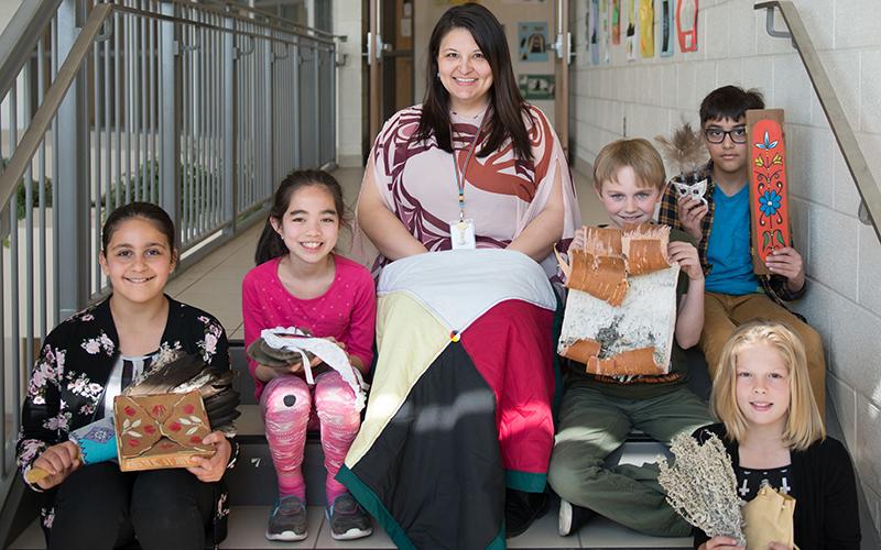teacher and students sitting on stairs displaying indigenous history projects