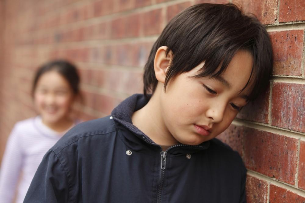 Elementary student leaning against brick wall looking sad or hurt