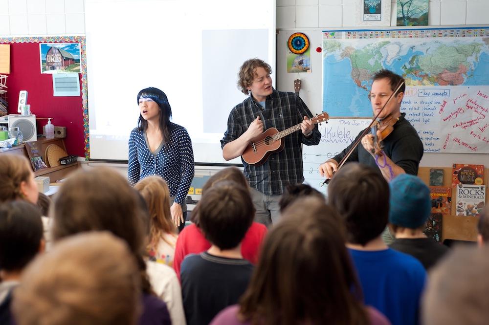 three musicians performing in front of classroom of elementary students