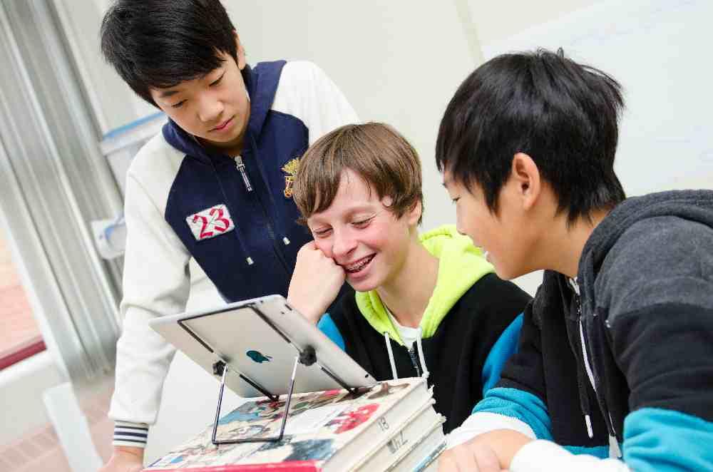 three students looking at tablet propped up on textbooks