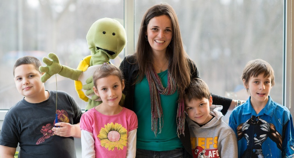 elementary students standing with teacher and puppet