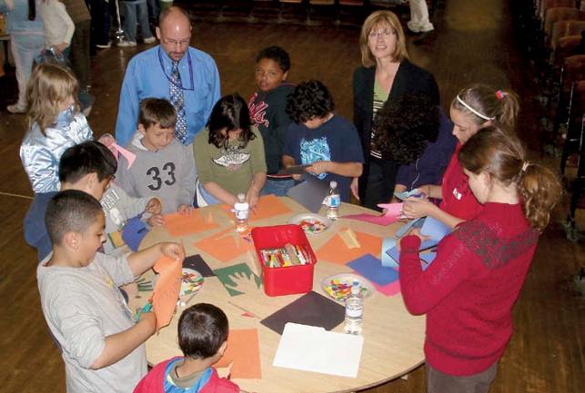 students standing at round table creating art from construction paper