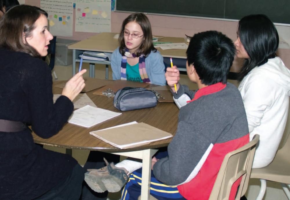 teacher sitting with three elementary students at a desk in classroom