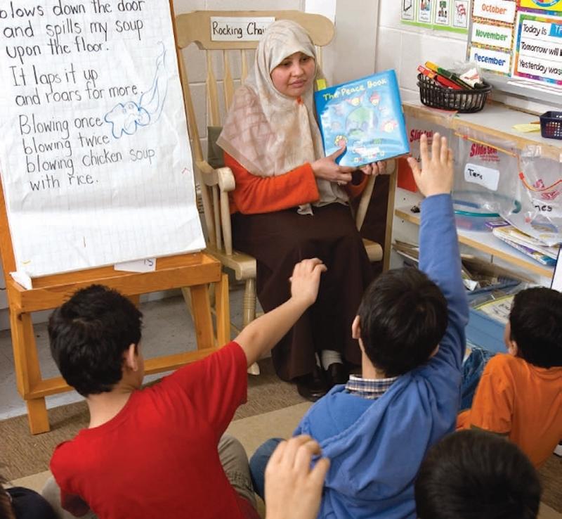 Teacher reading book to students with their hands up