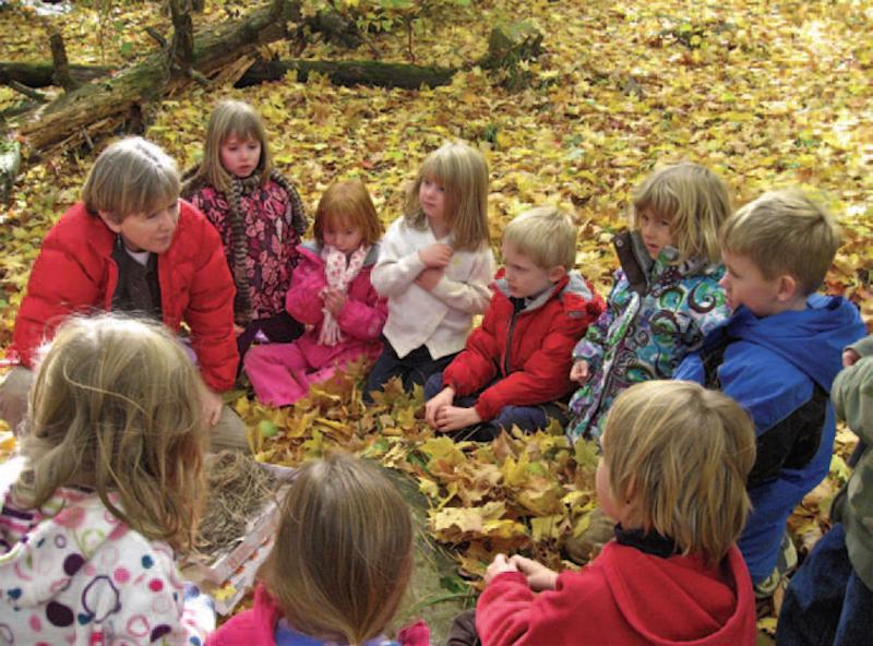teacher sitting with young students in a circle on top of leaves outside