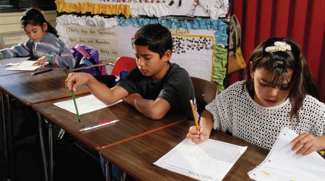 three students sitting at desks writing on paper