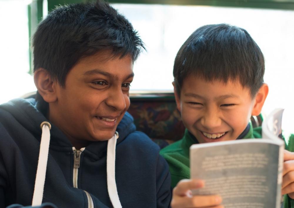 Two elementary students laughing while reading a book