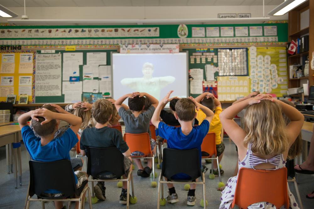 Young students facing projection with hands on heads