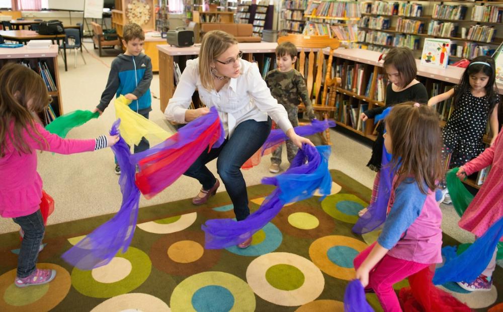Teacher dancing with elementary students holding colourful feathers