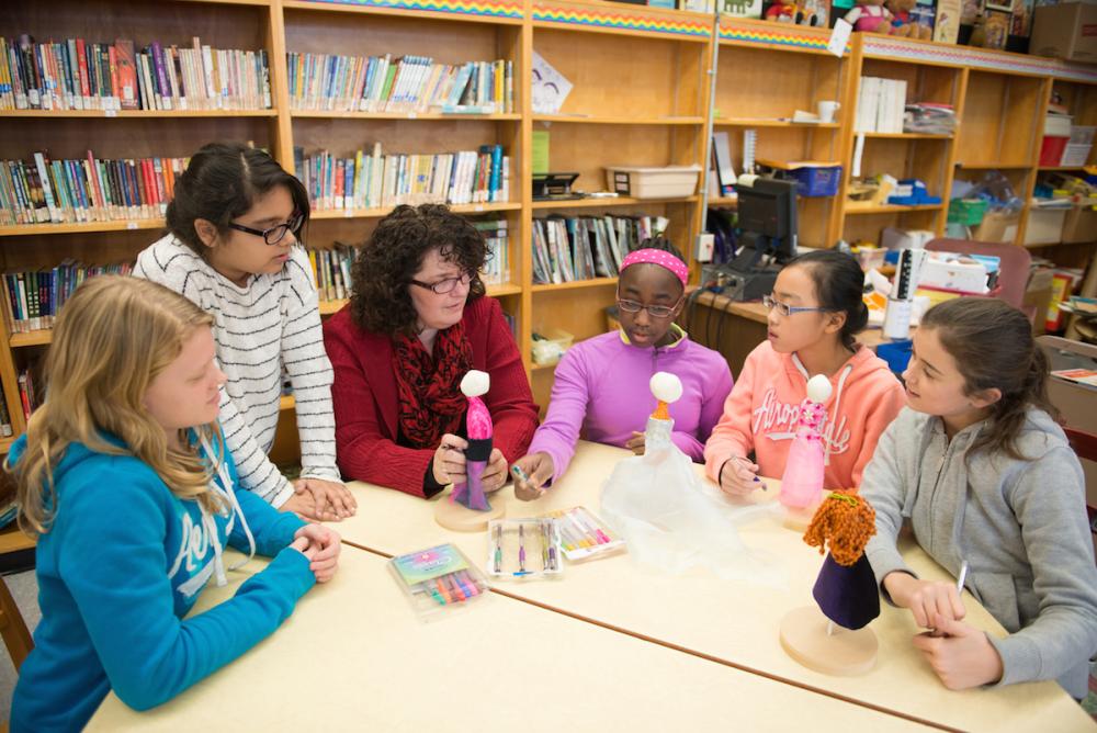 Elementary students and teacher sitting together working on dolls in library