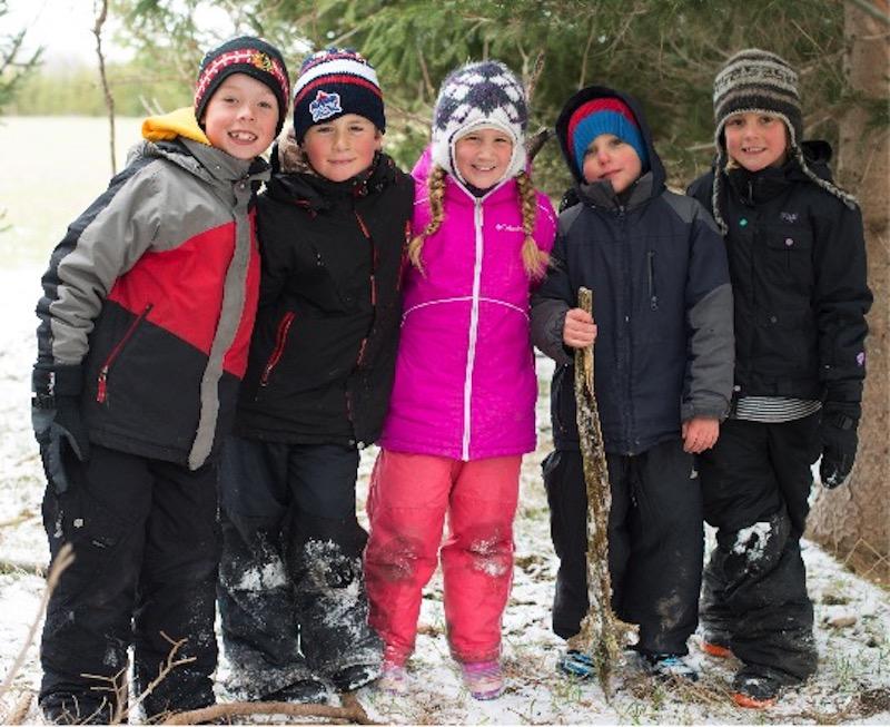Children wearing snowsuits standing near wooded area
