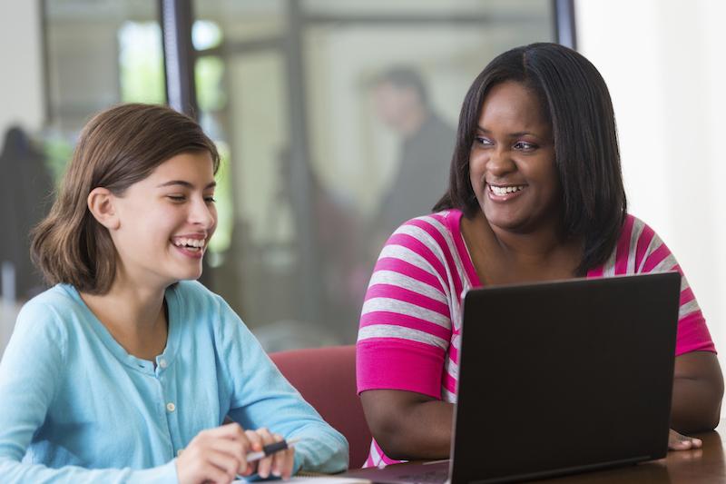 Teacher and student, smiling, looking at laptop 