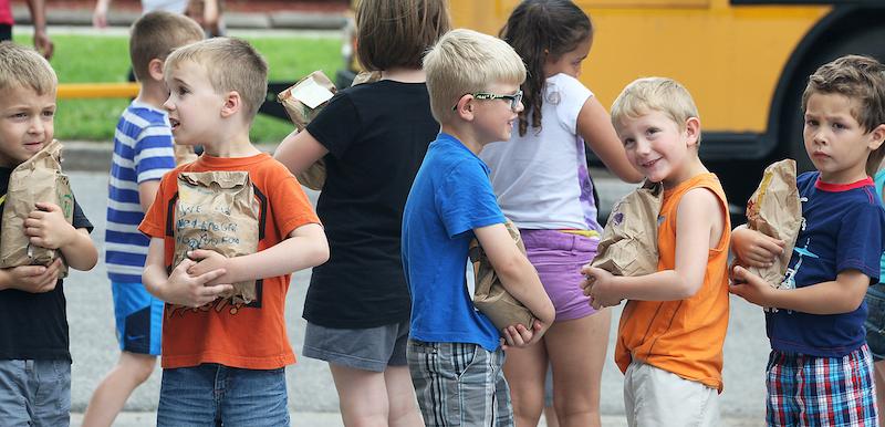young elementary students standing together near school bus holding paper bags