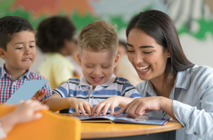 Woman teacher interacting with two kindergarten students with book