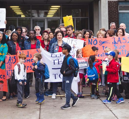 teachers and parents standing in front of school with signs