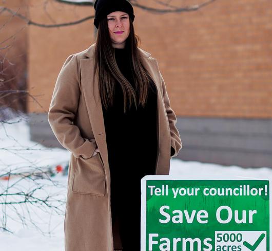 Sarah Lowes standing next to sign for saving farms