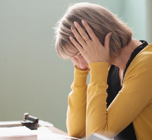 Woman with hands on head looking stressed while sitting in classroom