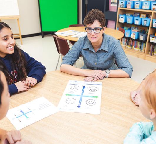 Sue Ducau sitting at table with elementary students