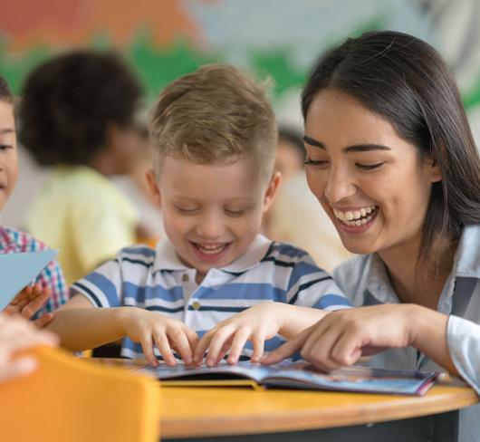 Woman teacher interacting with two kindergarten students with book