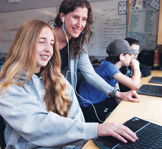 Two students sharing earbuds while looking at laptop
