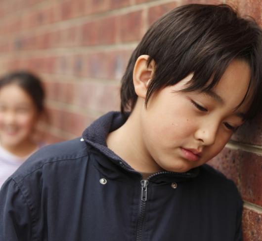 Elementary student leaning against brick wall looking sad or hurt