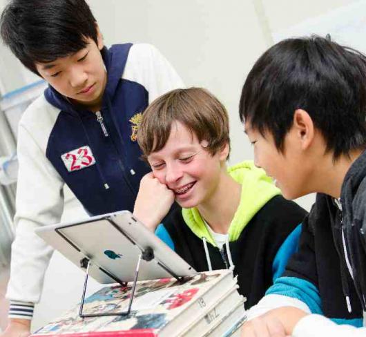 three students looking at tablet propped up on textbooks