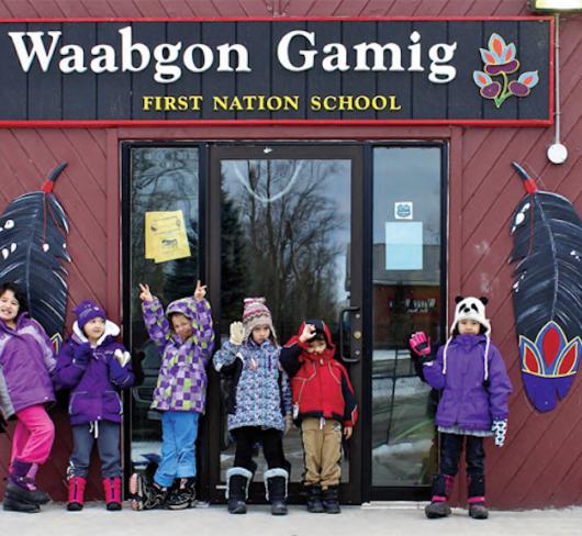 Young children in winter wear standing out front of Waabgon Gamig First Nation School