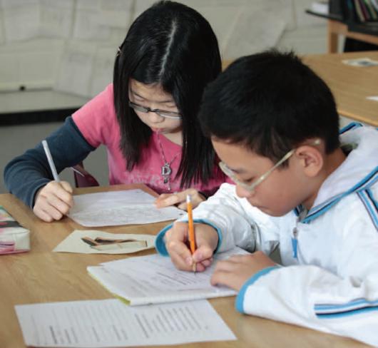 two students writing on paper with pencils in classroom