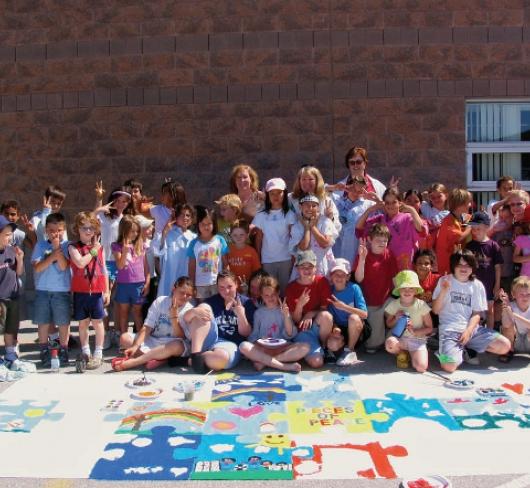 elementary class standing outside of school with artwork in front of them