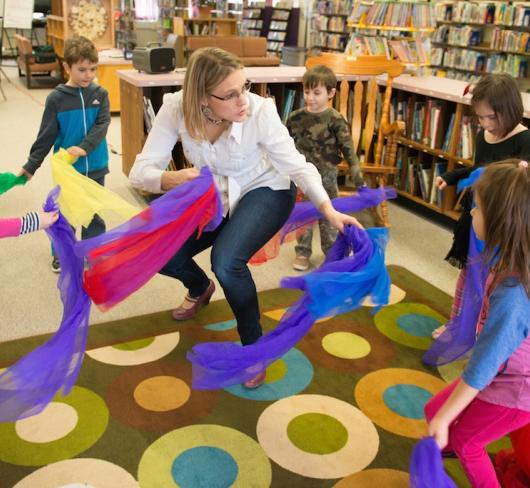 Teacher dancing with elementary students holding colourful feathers